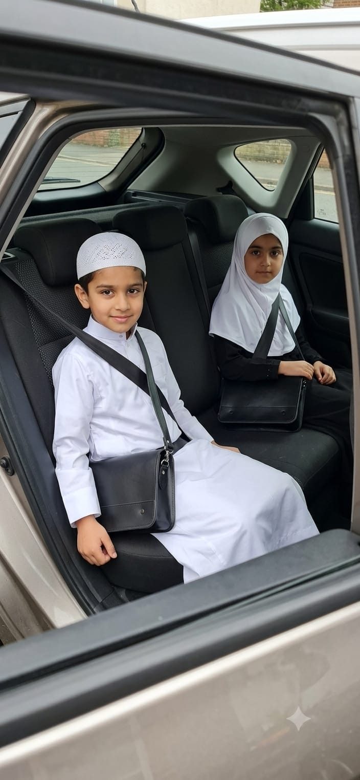 Two children in the back of a car on the madrasah run, each with a black leather madrasah bag (madrasa bag) on their lap