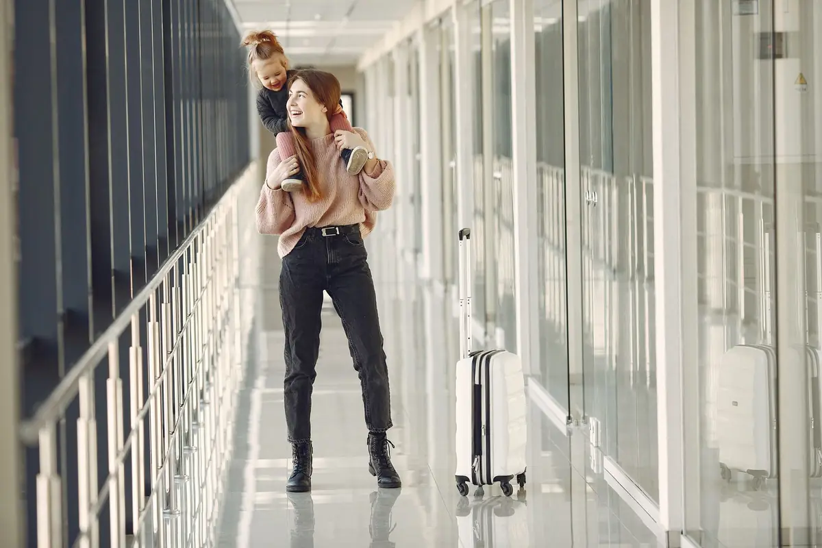 A mother carrying her child with a suitcase in a bright corridor