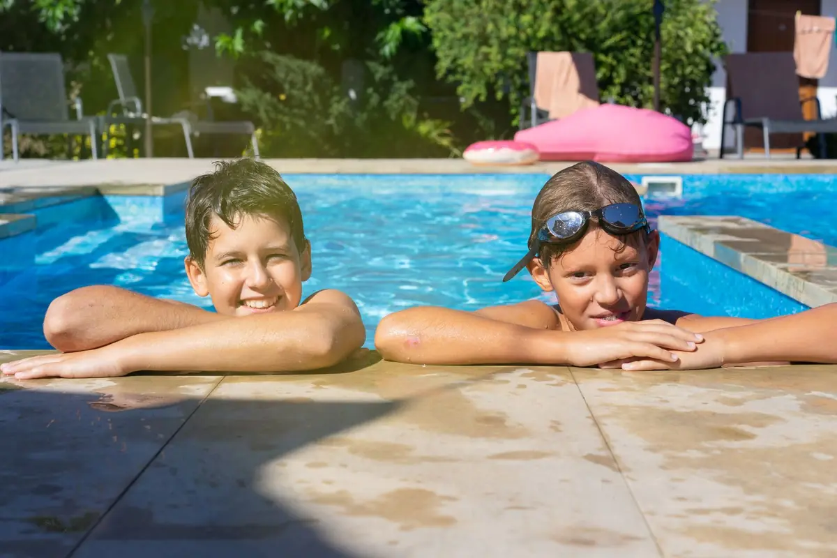 Two children smiling at the edge of a swimming pool