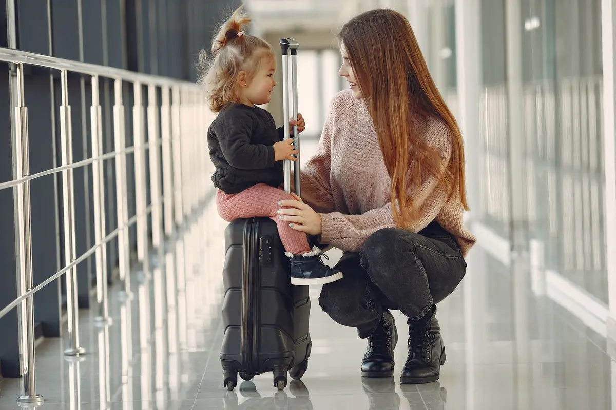 A mother crouching beside her toddler with luggage