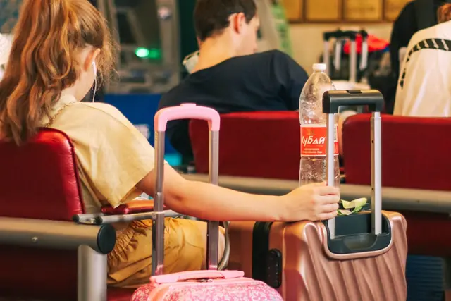 A traveller sitting beside a pink suitcase