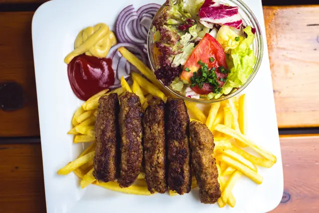 A plate of grilled ćevapi with chips and salad